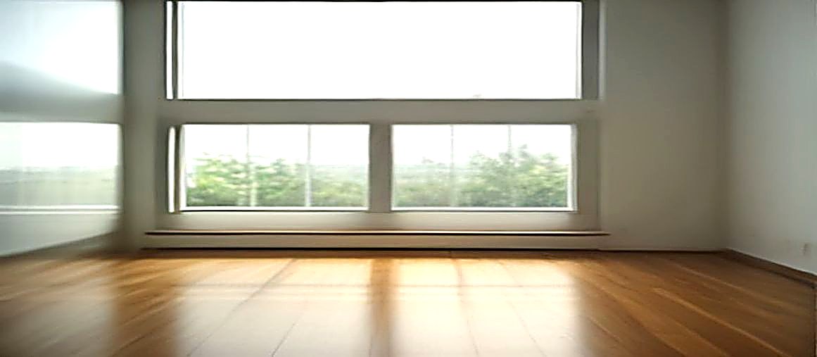큰 창 너머로 초록 나무와 환한 하늘이 보이고 빈 나무 바닥이 있다.